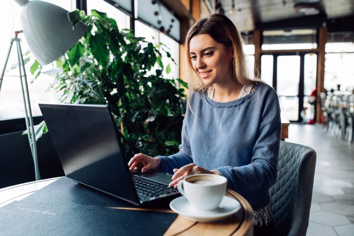 Frau sitzt im Café und tippt auf einem Laptop