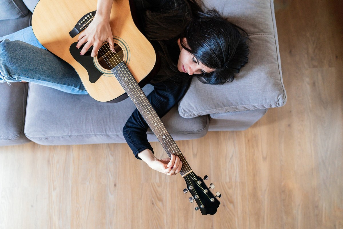 Frau liegt auf der Couch und spielt Gitarre