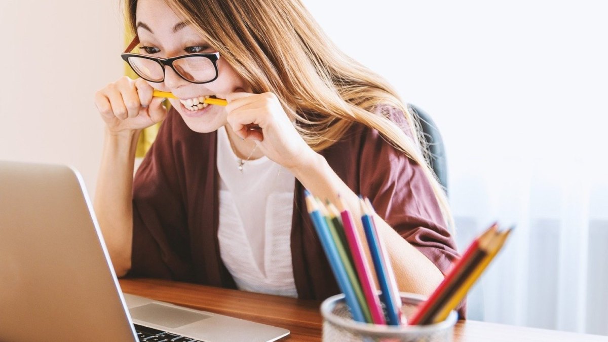 Eine Frau schaut auf ihren Laptop und beißt vor lauter Ärger in ihren Stift.