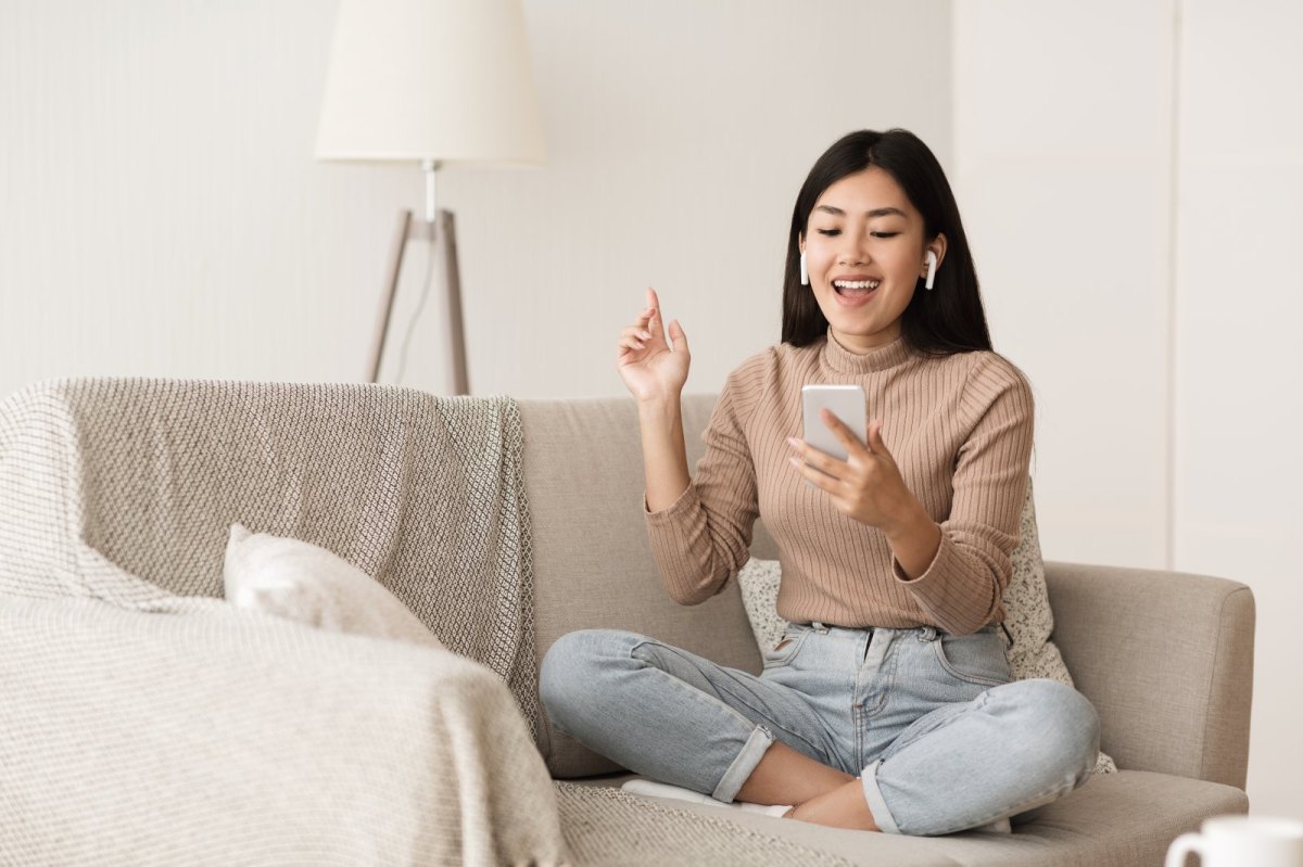 Frau sitzt auf dem Sofa und hat AirPods im Ohr.