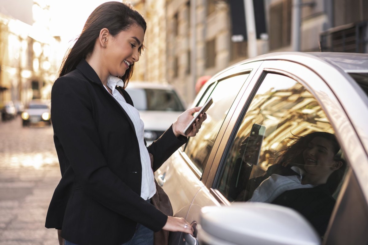 Frau mit Handy in der Hand vor einem Auto.