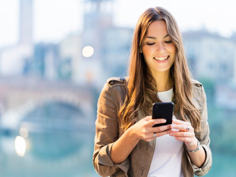 Frau schaut lächelnd auf ihr Handy.