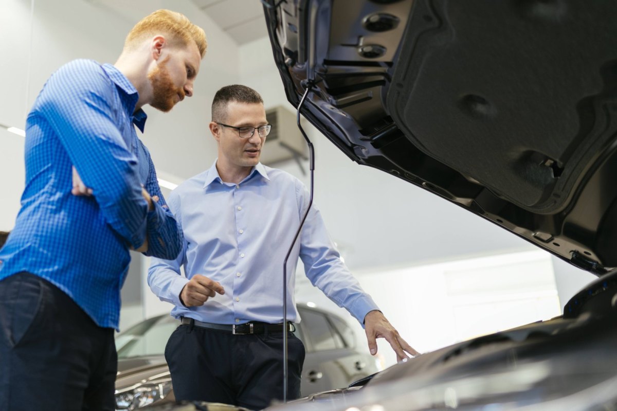 Verkäufer und Kunde in einem Autohaus schauen sich den Motor eines Wagens an.