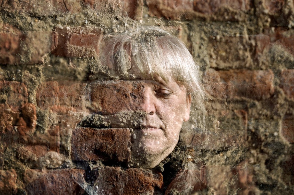 Eine Frau halb unsichtbar vor einer Backsteinmauer