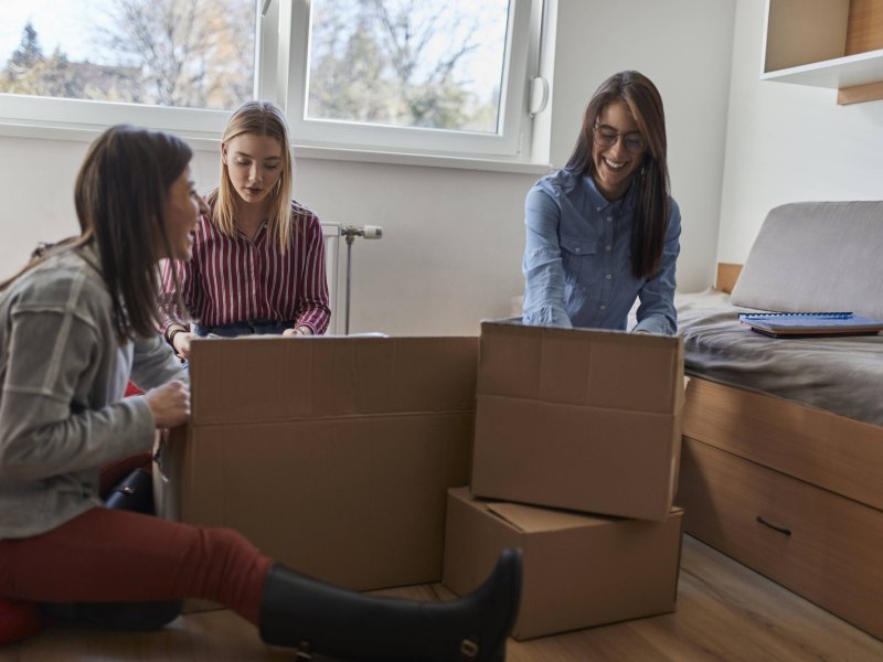 Drei junge Frauen packen Umzugskartons.