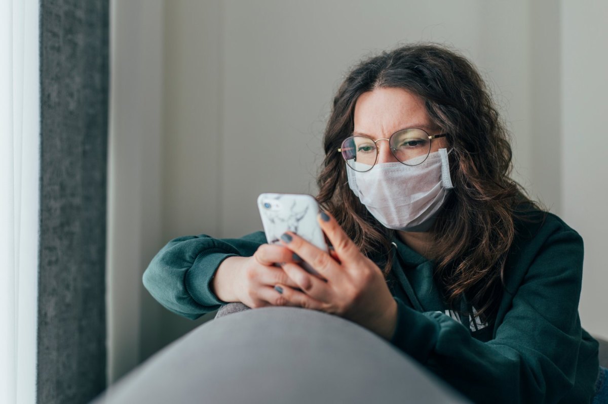 Frau mit Maske guckt auf ihr Handy.