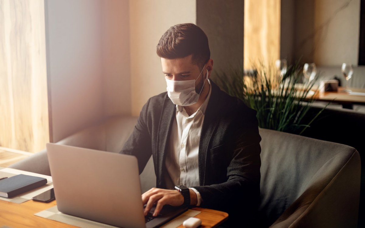 Mann sitzt mit Mundschutz vor einem Laptop.