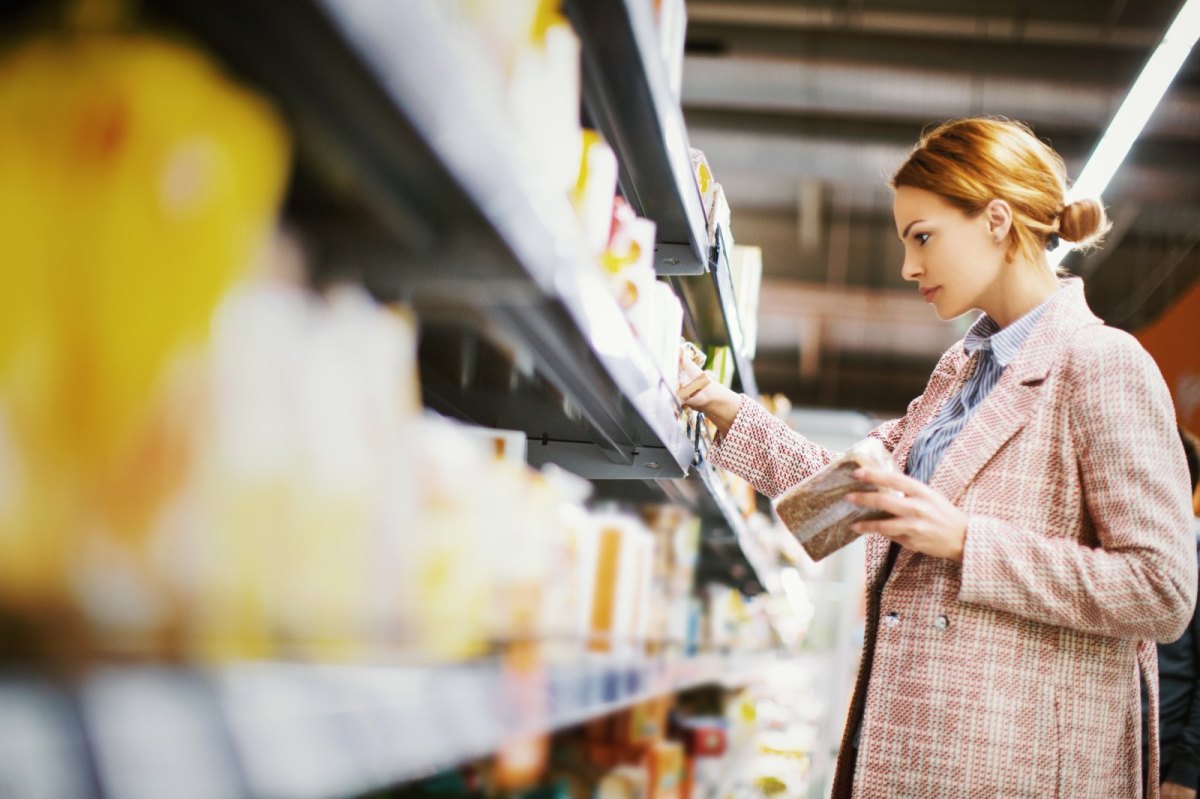 Junge Frau steht vor einem Regal im Supermarkt und hält eine Packung Vollkornbrot in der Hand.