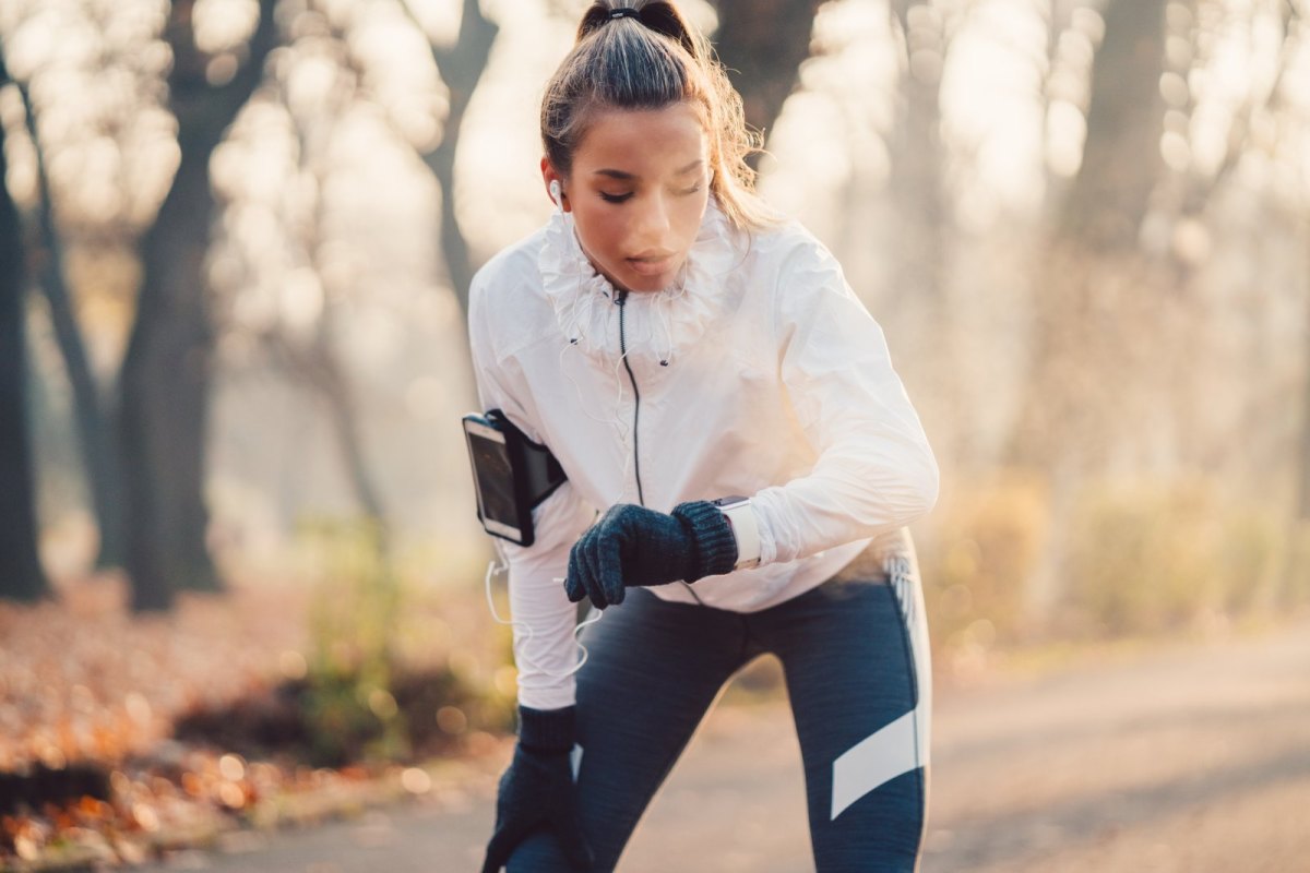 Frau schaut beim Joggen durch den Wald auf Fitness-Armband.