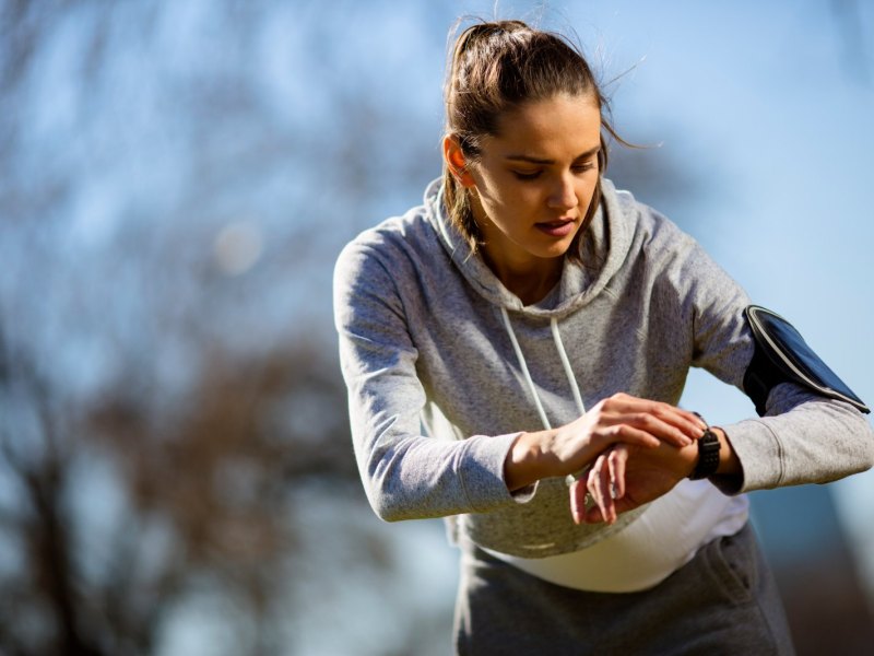 Junge Frau beim Joggen im Park guckt auf ihren Fitness-Tracker.