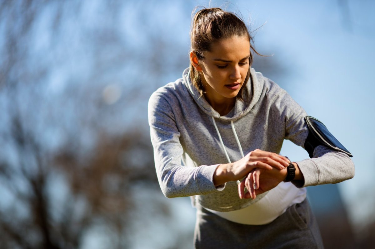 Junge Frau beim Joggen im Park guckt auf ihren Fitness-Tracker.