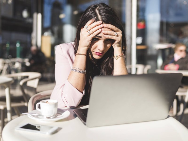 Frau sitzt geschockt vor ihrem Laptop im Café.