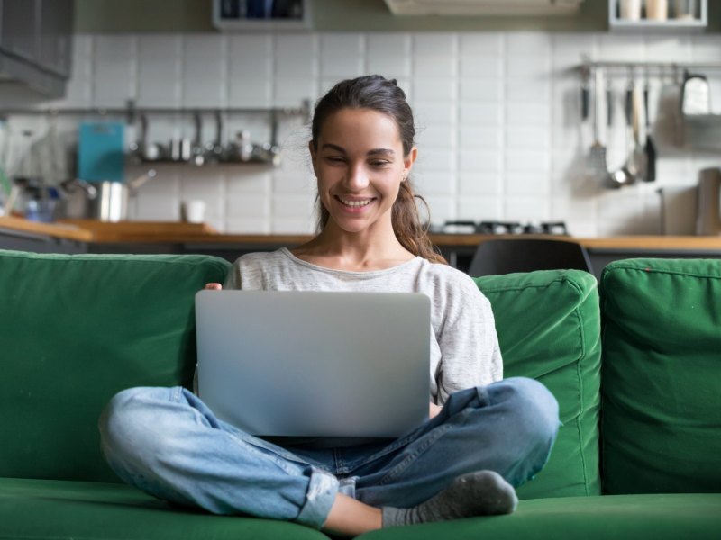 Frau sitzt auf einem grünen Sofa und hat einen Laptop auf dem Schoß.