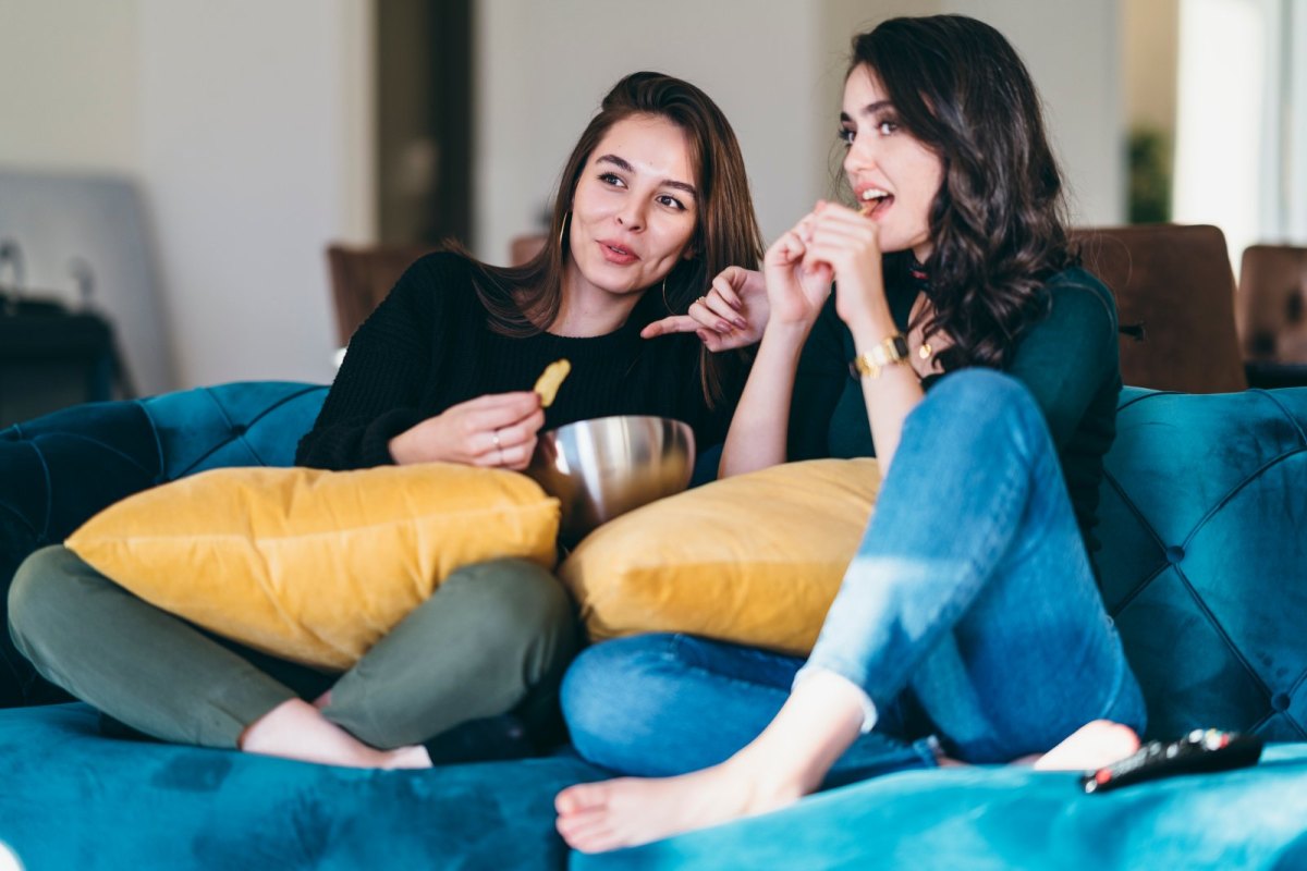 Zwei Frauen sitzen mit Chips vor dem Fernseher.