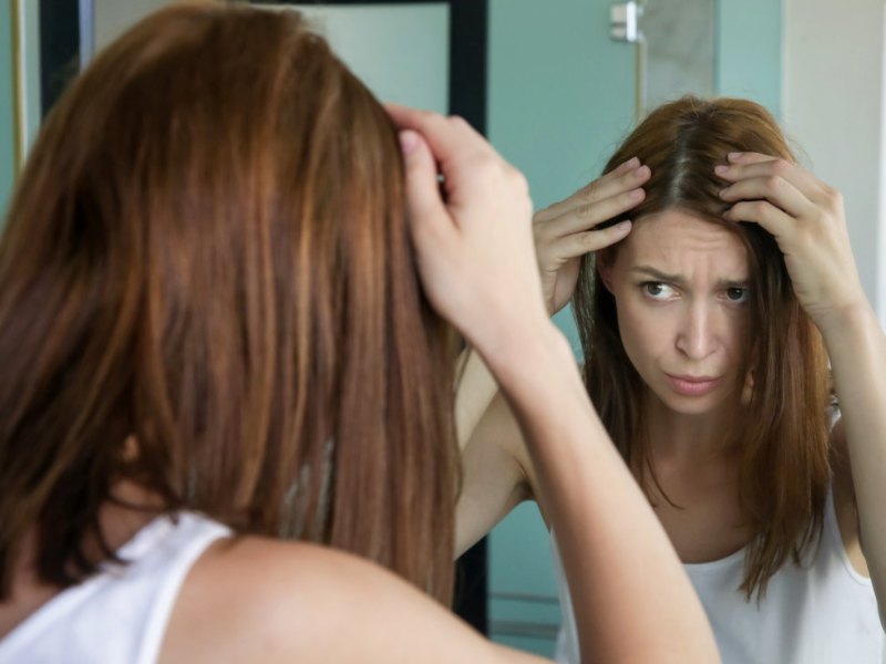 Junge Frau steht vor dem Spiegel und sieht graue Haare.