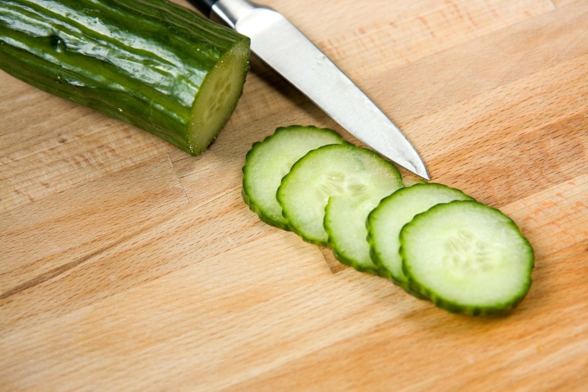 Eine Gurke in Scheiben geschnitten. Das Messer liegt daneben.