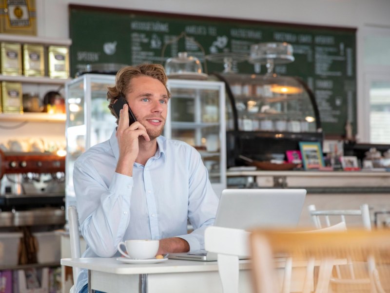 Mann sitzt im Café und telefoniert.