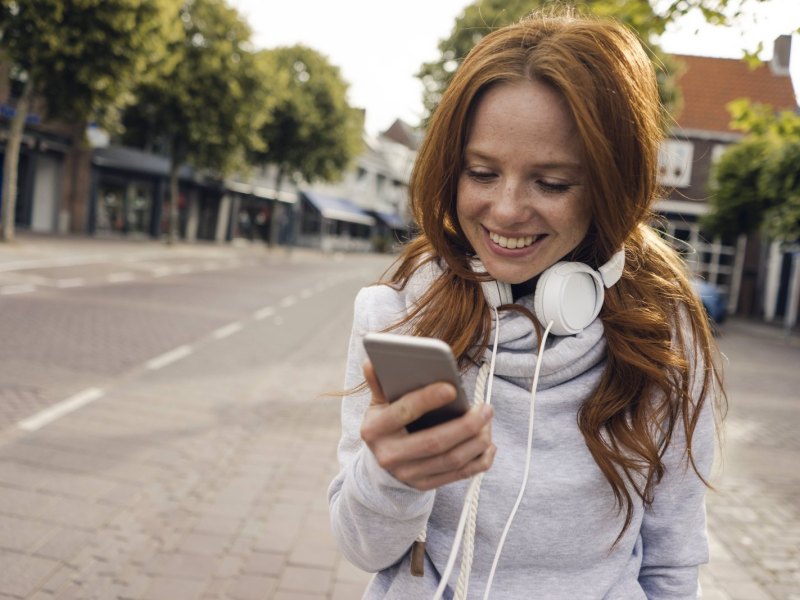 Eine Frau steht in der Stadt und schaut auf ihr Smartphone.