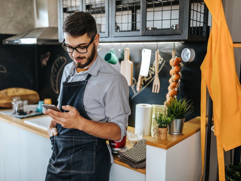 Mann steht mit Handy in der Küche.