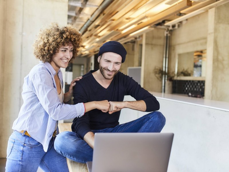 Mann und Frau geben sich eine Fistbump mit Laptop.