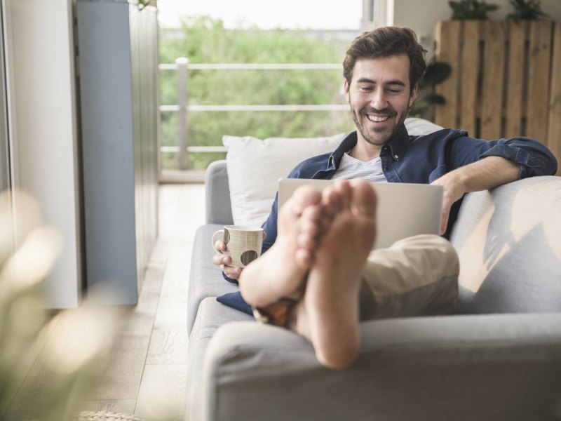 Mann mit Laptop auf Sofa.