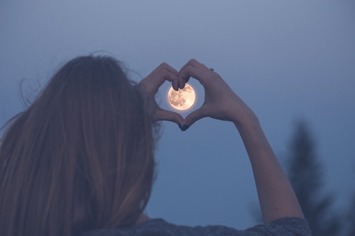 Frau umrahmt den Mond mit einem Herz