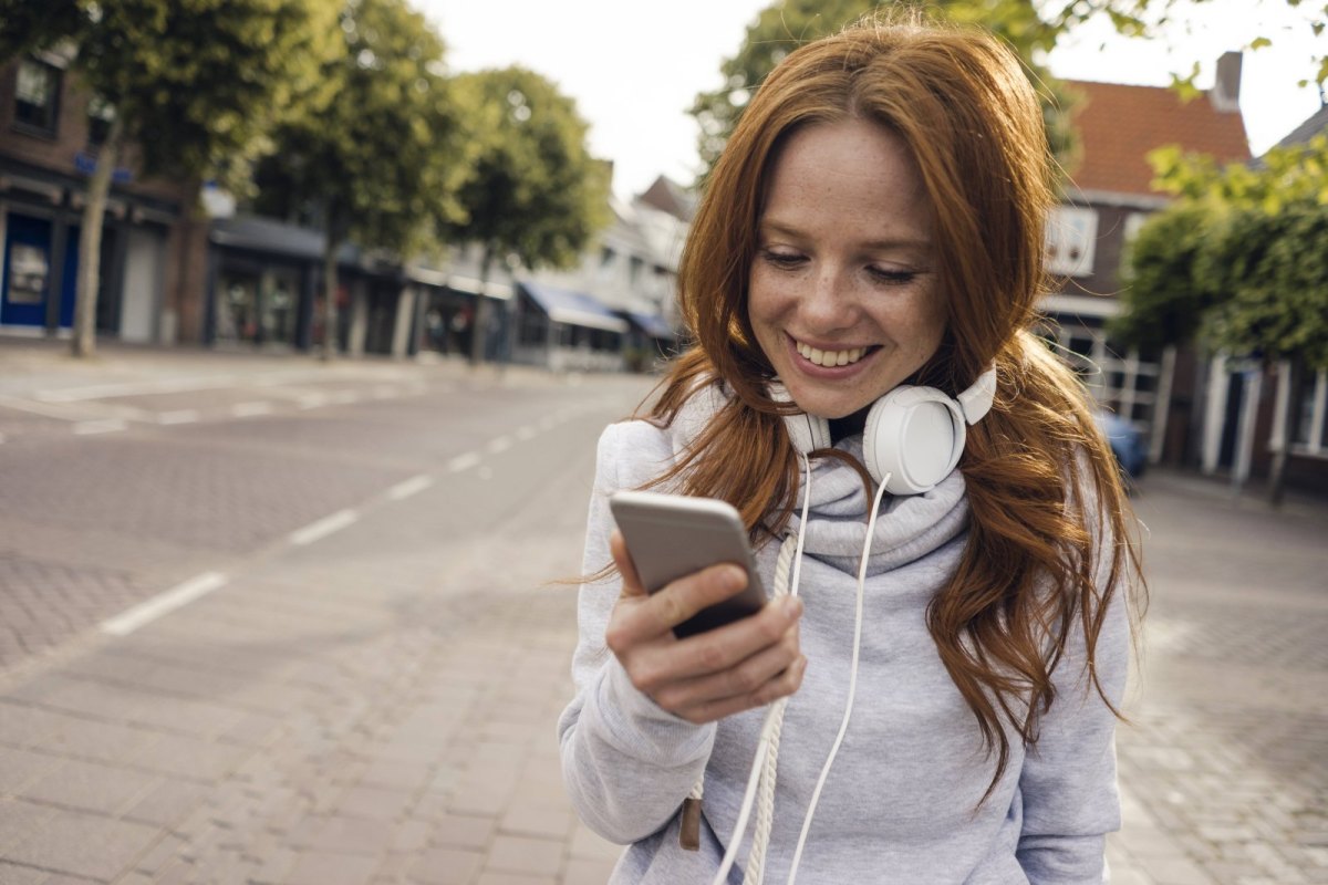 Eine Frau hört mit Kopfhörern auf ihrem Smartphone Musik.