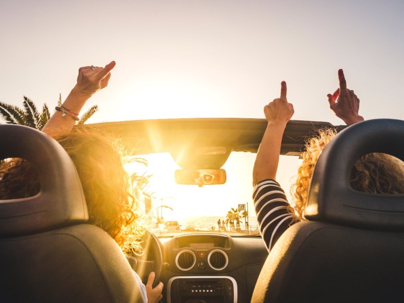 Menschen im Auto von hinten heben fröhlich die Arme in die Luft.