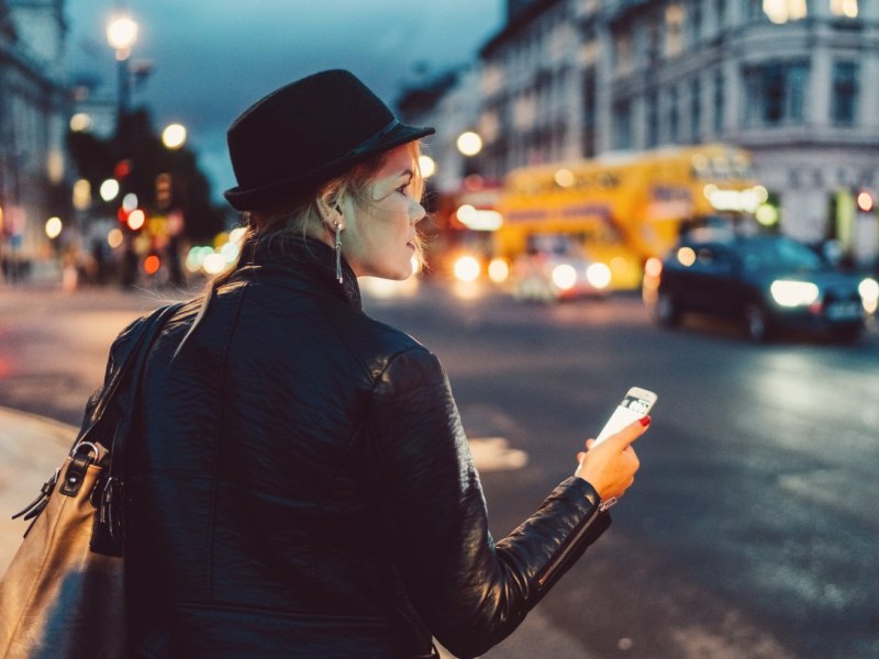 Frau mit Handy schaut sich in der Stadt um.