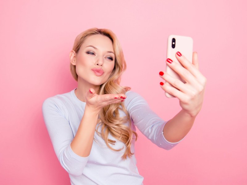 Frau macht Schmollmund und Handkuss für ein Selfie.