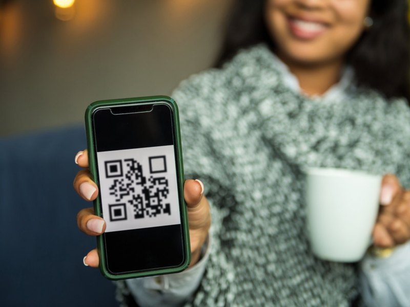 Frau hält Handy mit QR-Code auf dem Display in die Kamera.