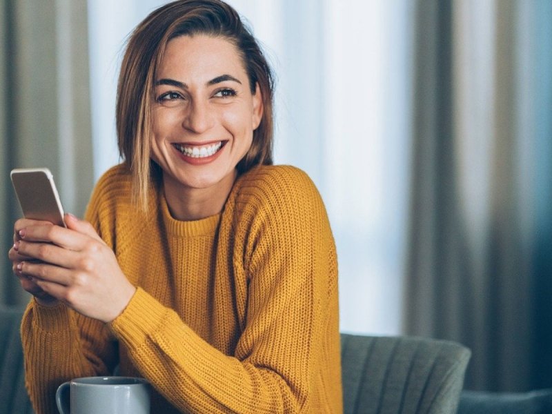 Eine Frau lacht und hält ihr Smartphone in den Händen.