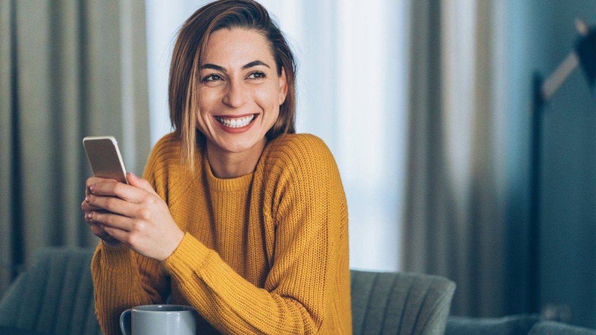 Eine Frau lacht und hält ihr Smartphone in den Händen.