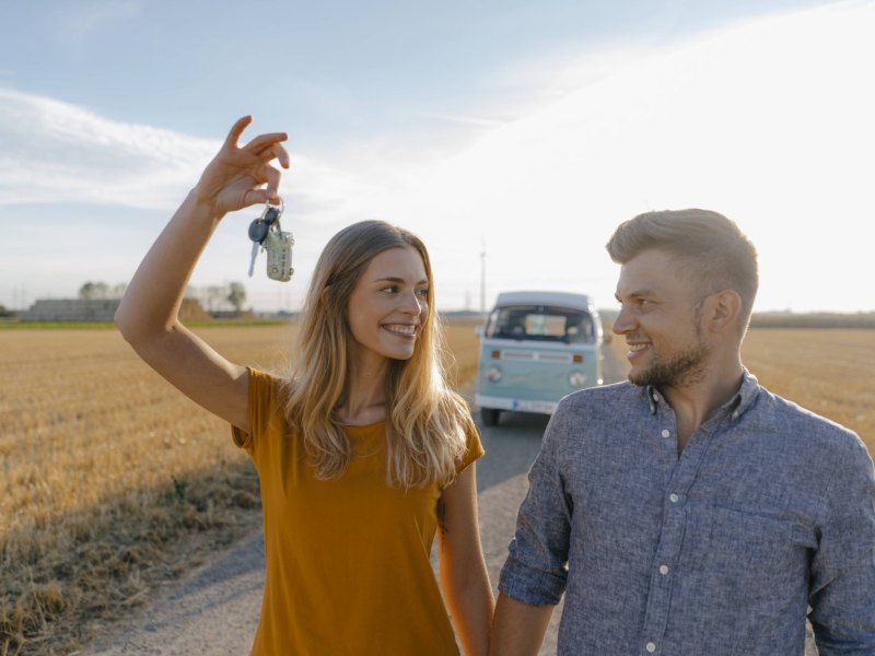 Eine Frau und ein Mann spazieren über ein Feld. Die Frau hält einen Schlüssel in die Luft.