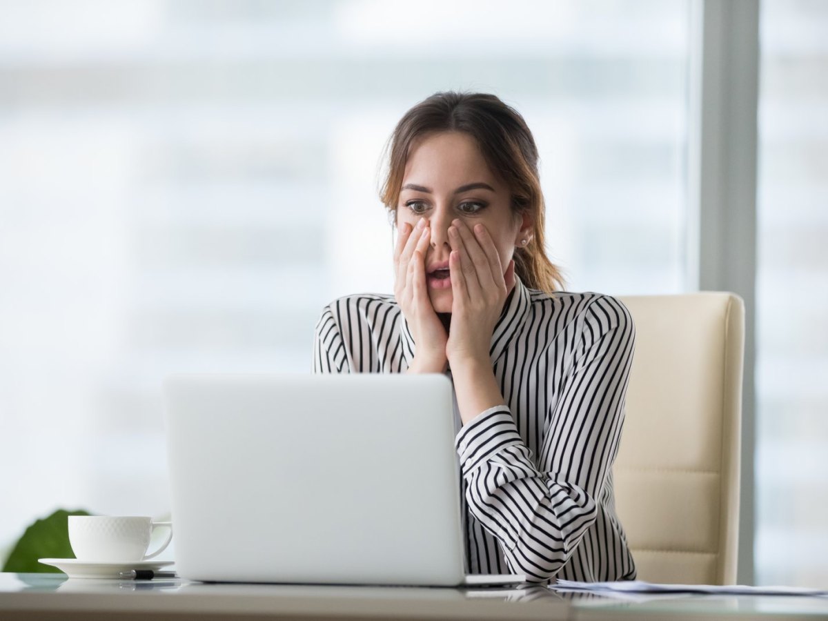 Junge Frau sitzt geschockt vor ihrem Laptop.