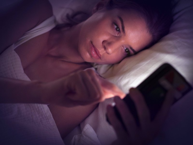 Eine Frau liegt im Bett und schaut auf ihr Smartphone.