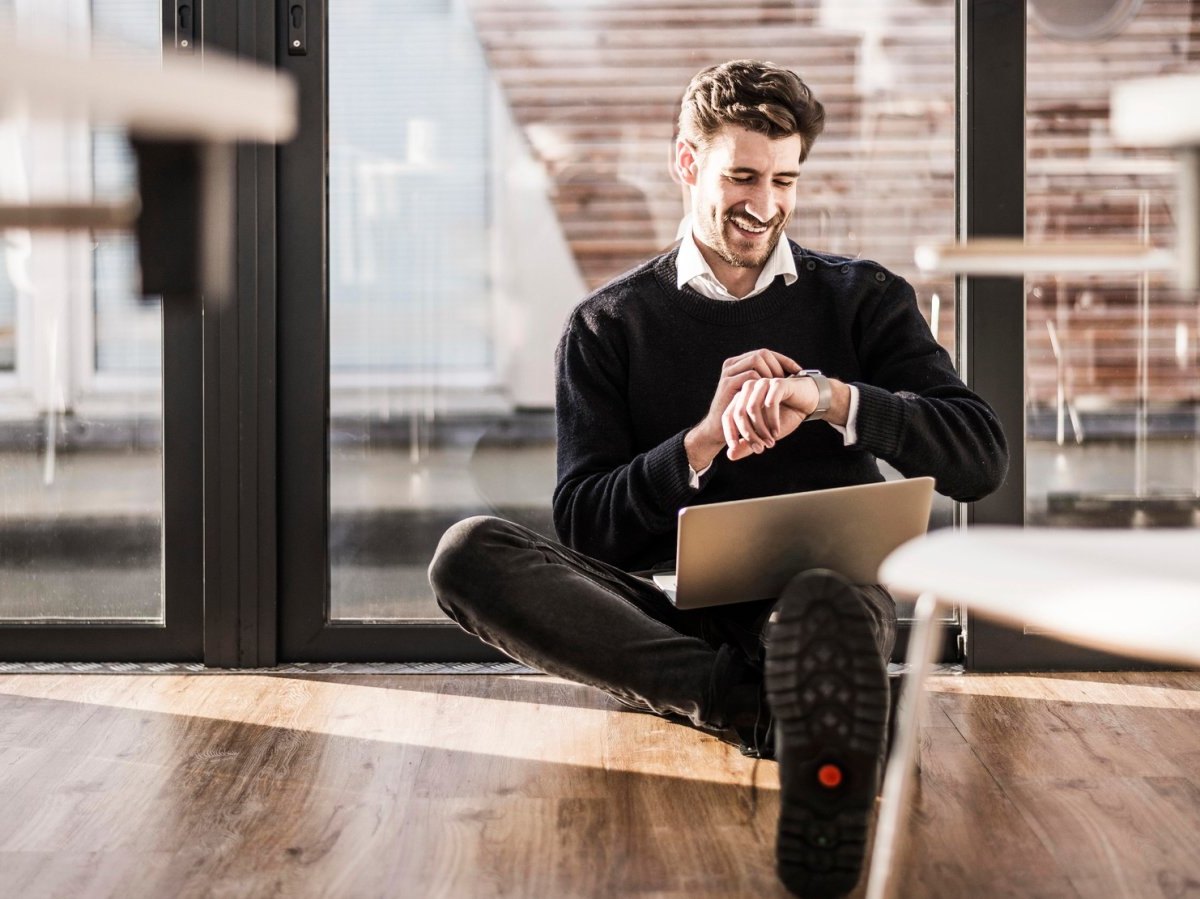 Mann mit Laptop und Smartwatch sitzend.