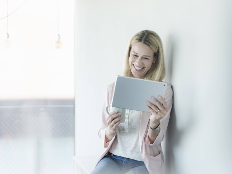 Frau lacht mit Tablet in der Hand.