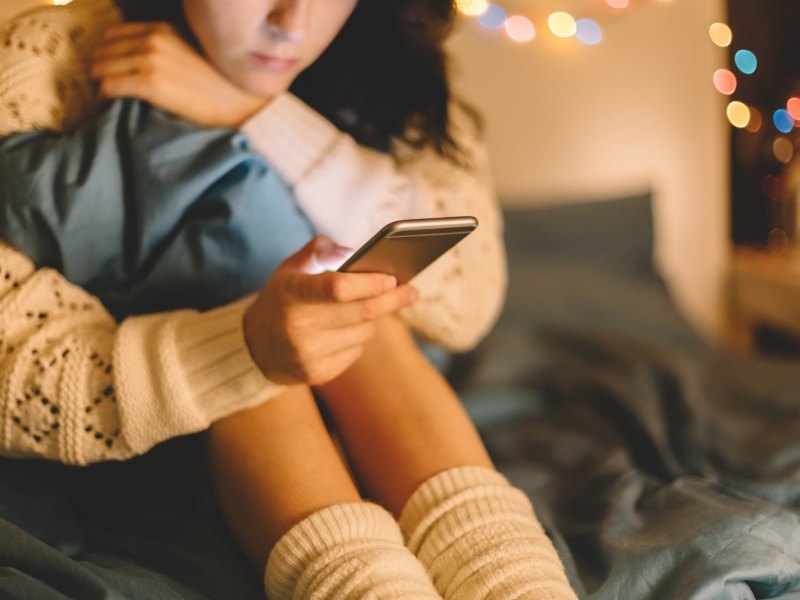 Frau sitzt mit Handy im Bett