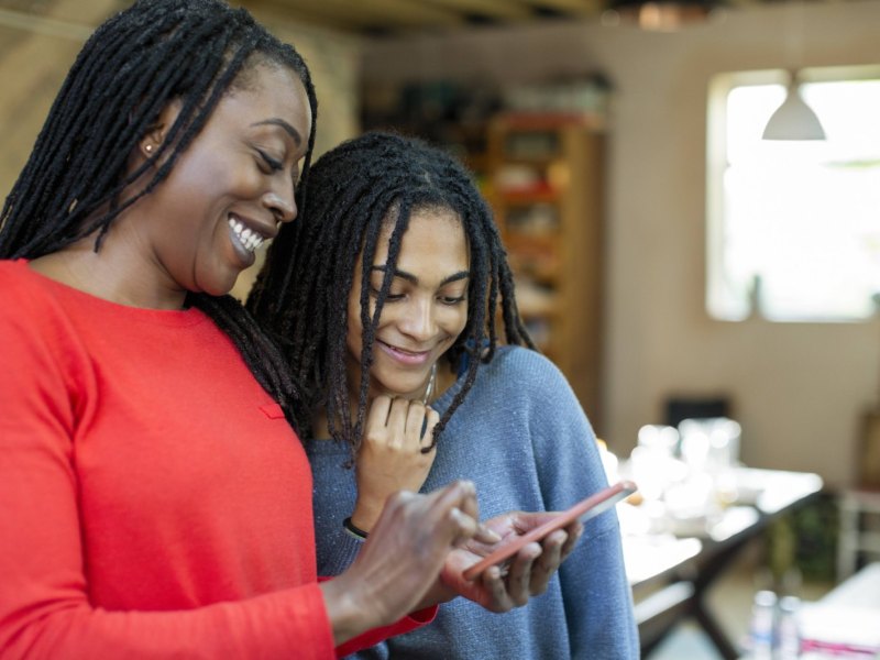 Zwei lachende Frauen schauen ein Video auf ihrem Smartphone.