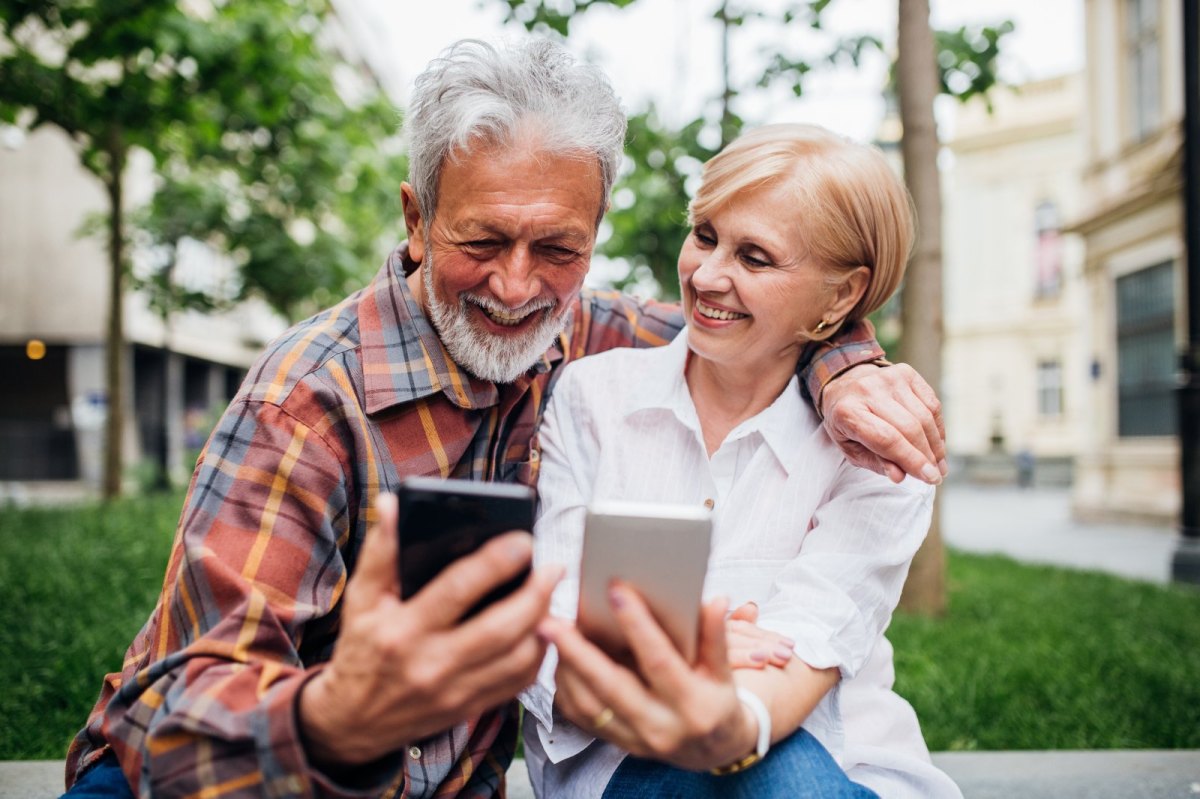 Ein älteres Paar schaut glücklich auf ihre Smartphones.