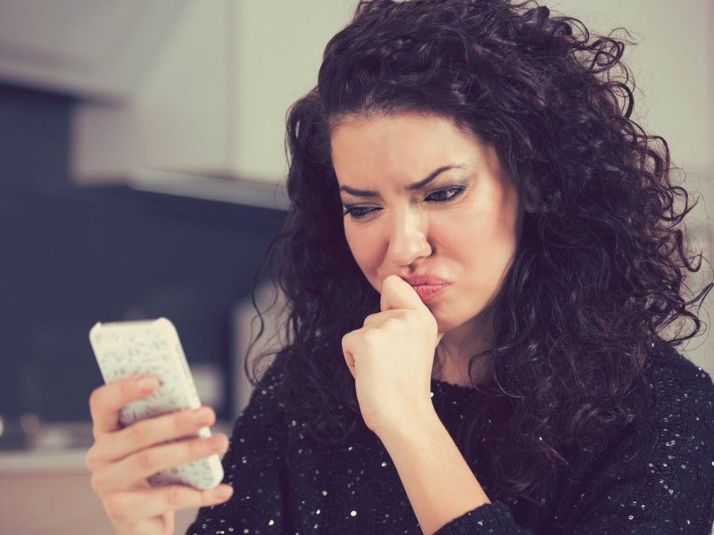 Frau blickt skeptisch auf ihr Handy.