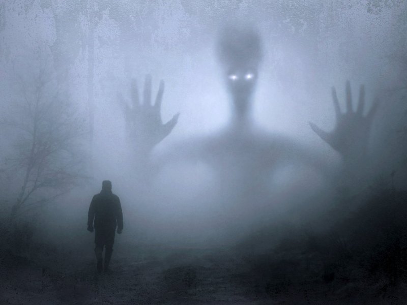 Mensch steht im Nebel vor einer großen Alien-Silhouette.