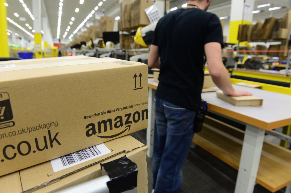 Mann in Logistikzentrum von Amazon mit Amazon-Paket im Vordergrund