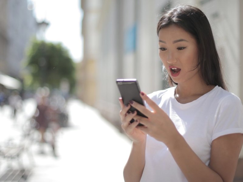 Eine Frau schaut erstaunt auf ihr Smartphone.