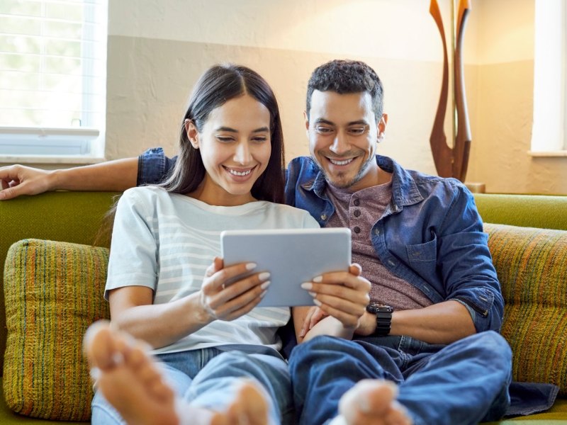 Ein Pärchen auf dem Sofa blickt auf ein Tablet.