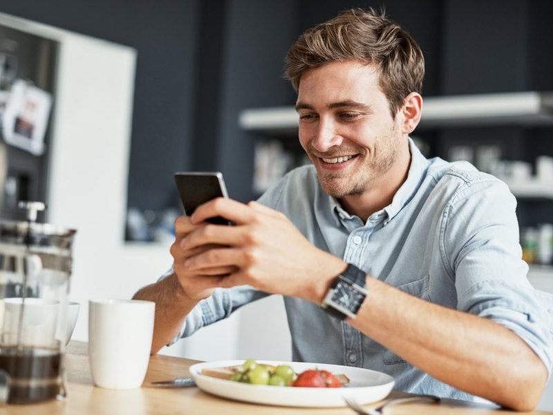 Mann blickt glücklich aufs Handy.