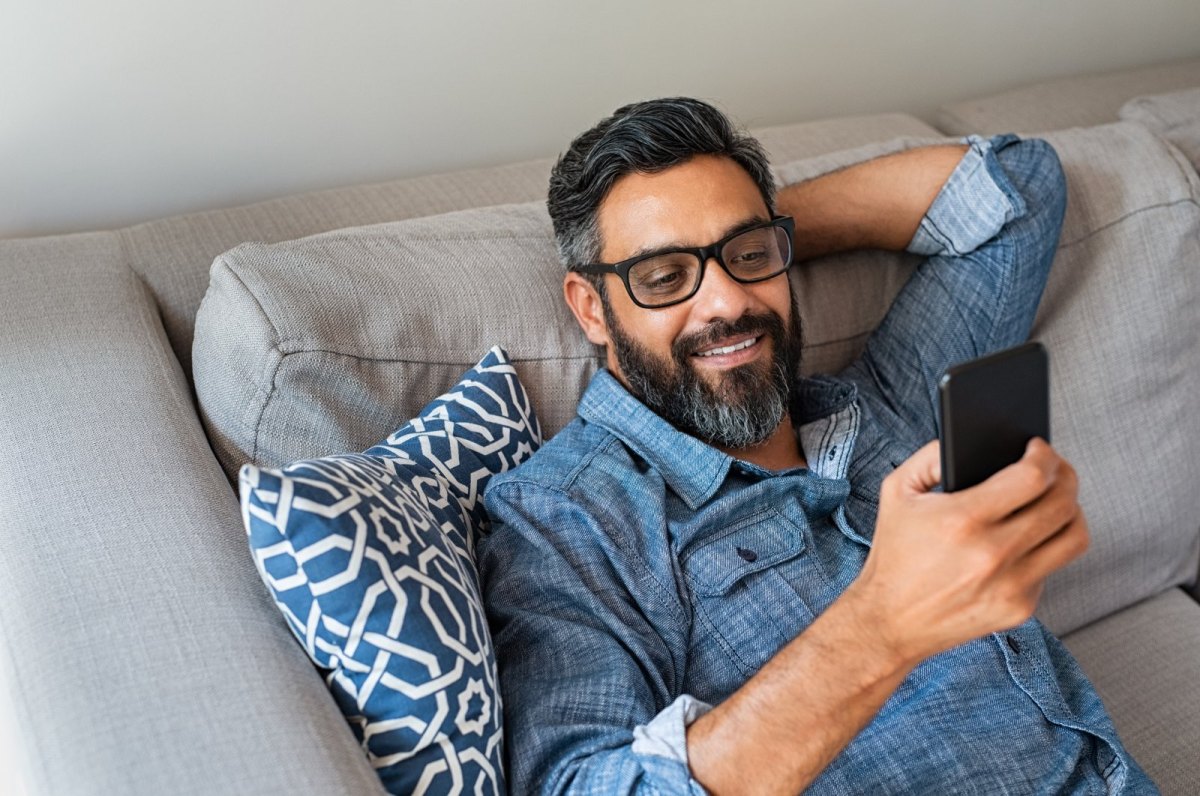 Mann auf dem Sofa blickt auf sein Handy.