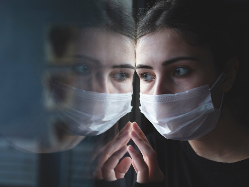 Frau mit Maske spiegelt sich im Fenster