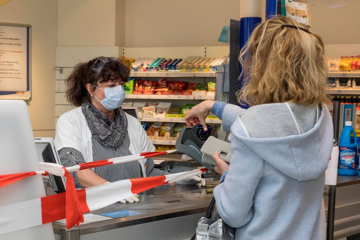 Eine Frau bezahlt mit Karte in einem Geschäft. Eine Kassiererin mit Mundschutzt sitzt vor ihr.